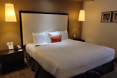 King size bed in hotel room with modern yellow lamp on each side of bed.